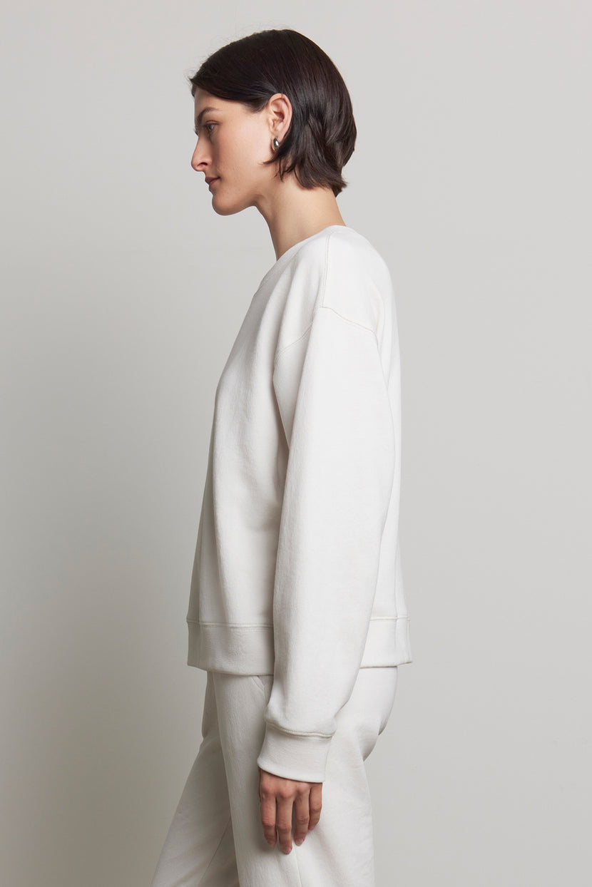 A person with short brown hair is wearing the YNEZ SWEATSHIRT from Velvet by Jenny Graham, along with matching pants, crafted from organic cotton, standing sideways against a plain background.