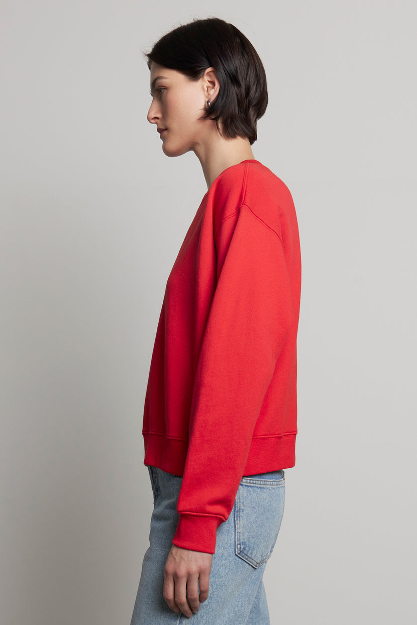 A person in a YNEZ sweatshirt by Velvet by Jenny Graham and blue jeans, standing in profile against a plain background, highlighting the elegance of sustainable fashion.