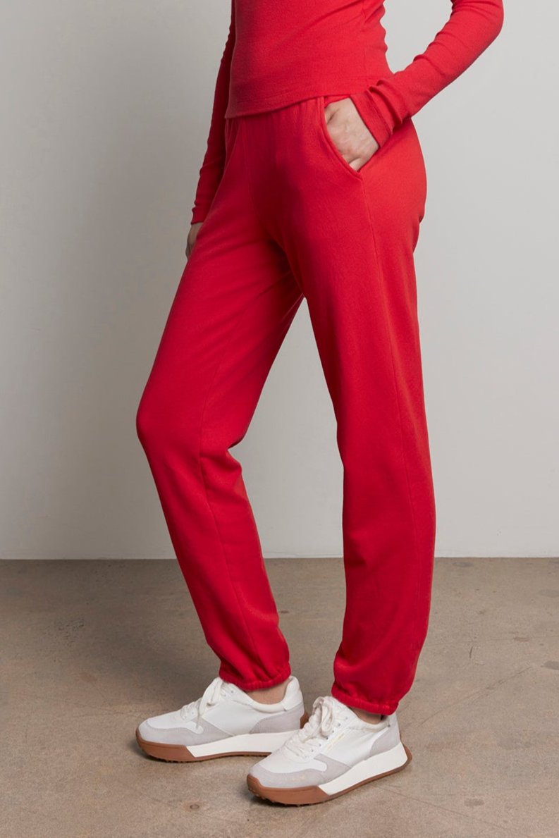   A person dressed in a red turtleneck and Velvet by Jenny Graham's ZUMA SWEATPANT poses against a plain backdrop, capturing the spirit of sustainable fashion. 