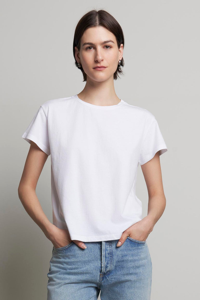 A person with short dark hair stands with hands in pockets, wearing a relaxed-fit TOPANGA TEE from Velvet by Jenny Graham made from organic cotton and light blue jeans.