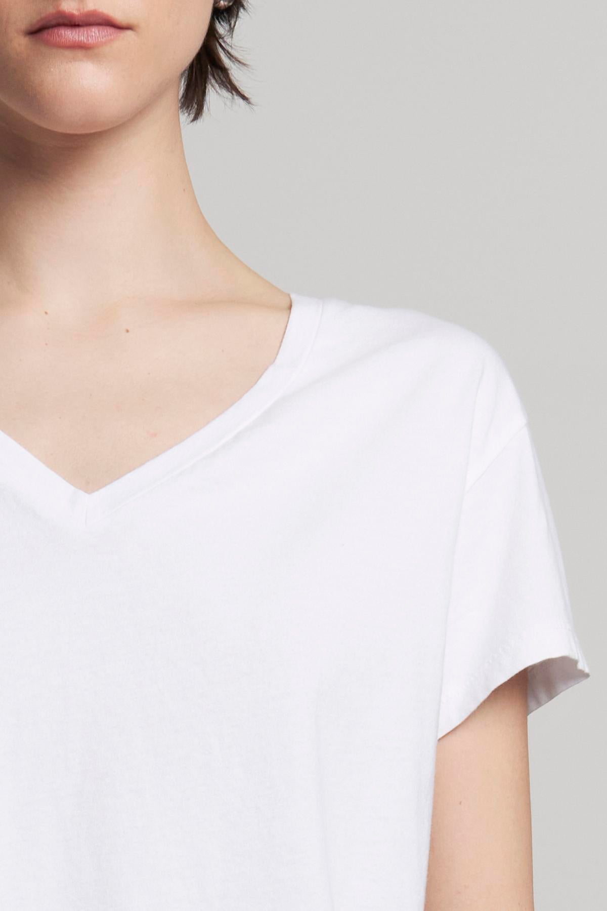   A person in a white VENICE TEE by Velvet by Jenny Graham stands against a neutral background, partially visible from the shoulders up. The organic cotton V-neck T-shirt nods subtly to classic 90s silhouettes. 