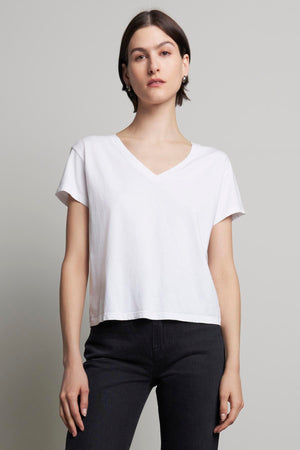 A person wearing the VENICE TEE by Velvet by Jenny Graham, paired with dark jeans, stands in front of a plain gray background.