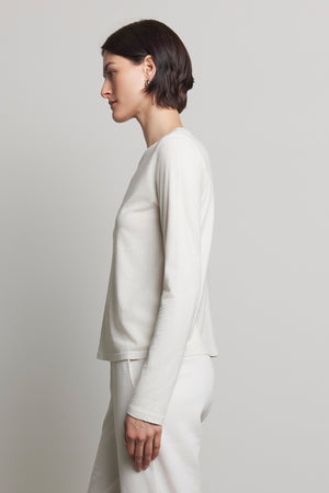 A person with short dark hair, dressed in a relaxed fit VICENTE TEE by Velvet by Jenny Graham and pants, stands in profile against a plain background.