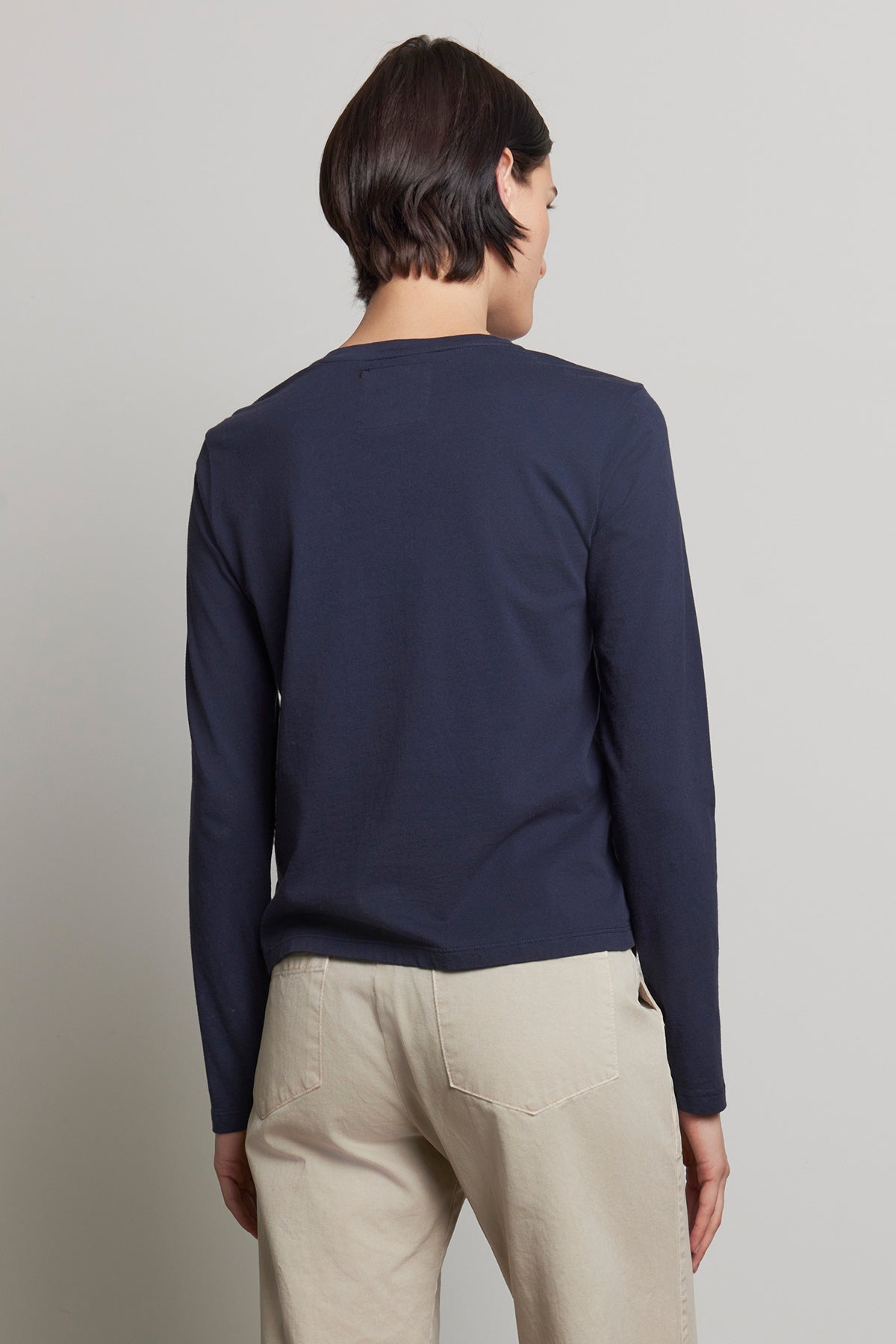   A person is seen from the back, wearing a relaxed fit navy VICENTE TEE by Velvet by Jenny Graham along with beige pants. 