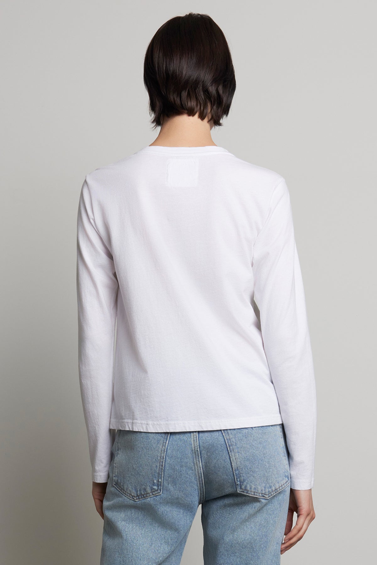 A person is seen wearing the relaxed-fit VICENTE TEE by Velvet by Jenny Graham, a white long sleeve shirt made of organic cotton, paired with blue jeans, and facing away from the camera.-38866410045633