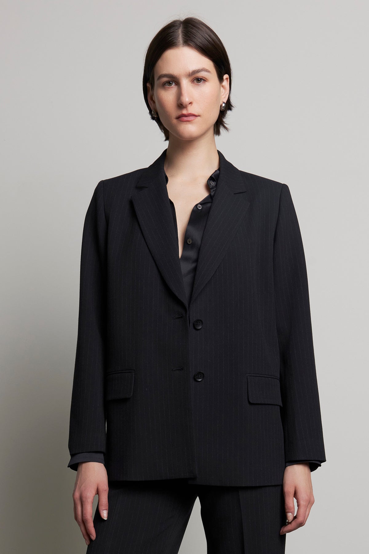   A person wearing the FRESNO PINSTRIPE BLAZER from Velvet by Jenny Graham, paired with a black shirt, stands against a plain background. 