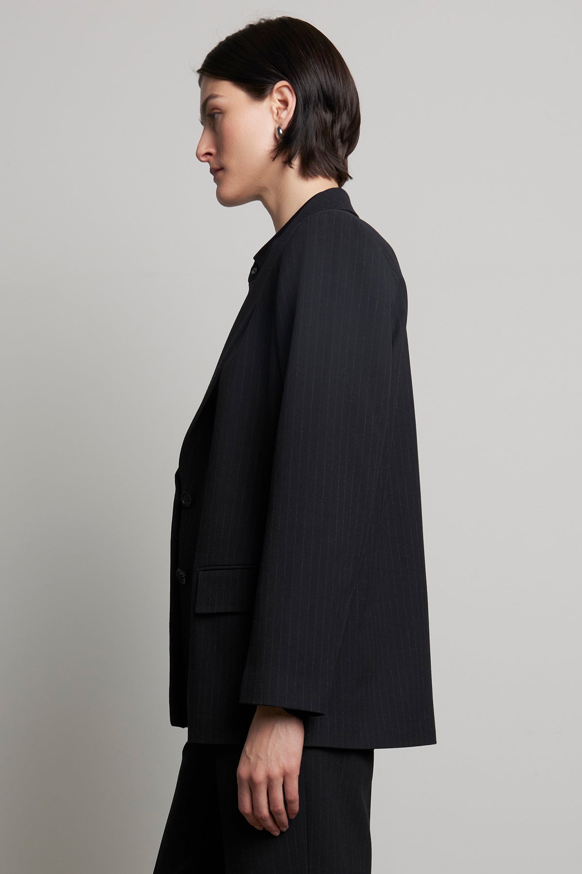   A person with short dark hair is wearing the FRESNO PINSTRIPE BLAZER from Velvet by Jenny Graham, featuring a notched collar, and is shown in side profile against a plain background. 