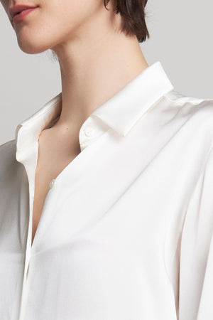 Close-up of a person wearing the CALABASAS SILK CHARMEUSE BLOUSE by Velvet by Jenny Graham, featuring its elegant drape and open collar design.