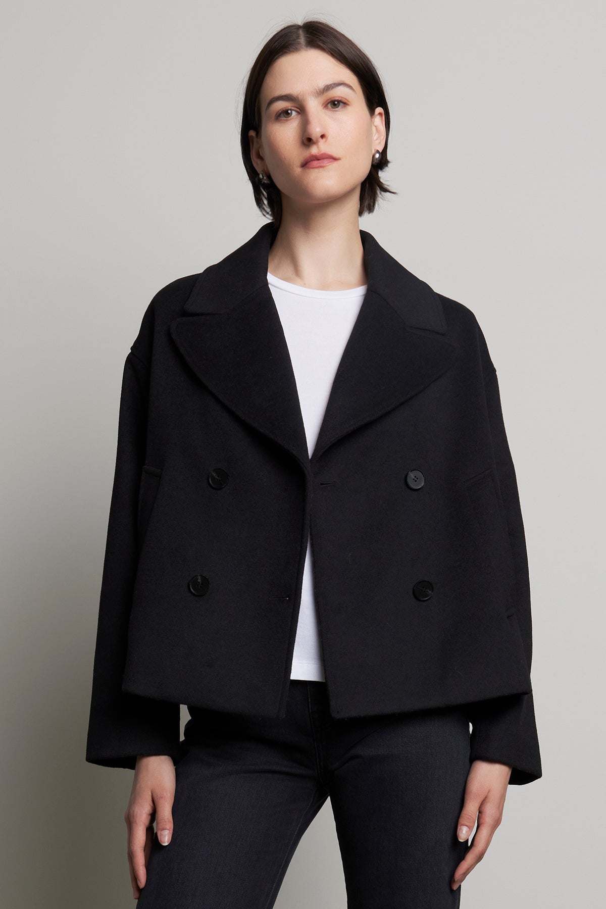   A person wearing the WESTWOOD PEACOAT by Velvet by Jenny Graham over a white shirt and dark pants stands against a plain background, exuding timeless appeal. 