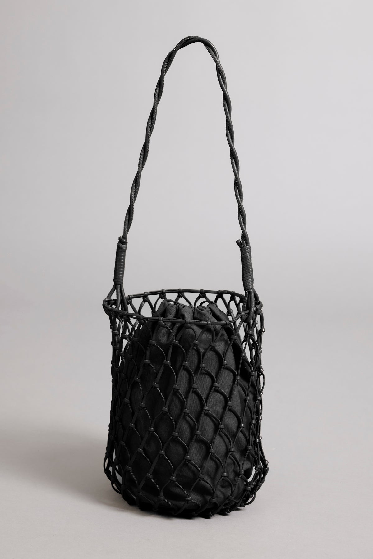   A black Velvet by Graham & Spencer mesh tote bag with a braided vegan leather strap and cinched top, standing against a plain light background. 