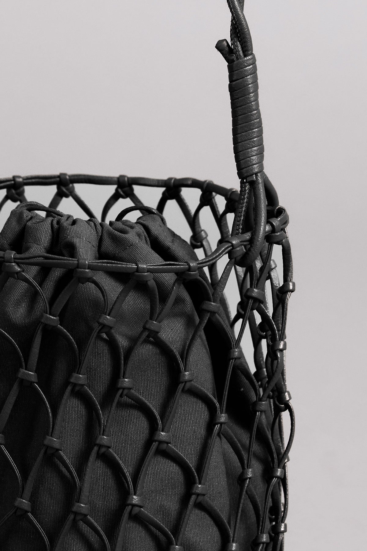   Close-up of a black Velvet by Graham & Spencer mesh tote bag containing a textured item, with a focus on the tightly interwoven, knotted details of the mesh design. 