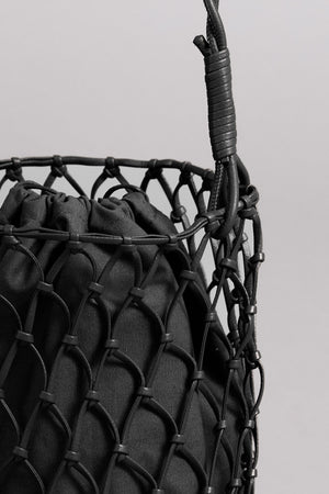 Close-up of a black Velvet by Graham & Spencer mesh tote bag containing a textured item, with a focus on the tightly interwoven, knotted details of the mesh design.