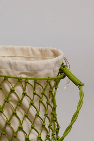 Close-up of a beige Velvet by Graham & Spencer MESH TOTE BAG with a green mesh design overlay and a green handle against a gray background.