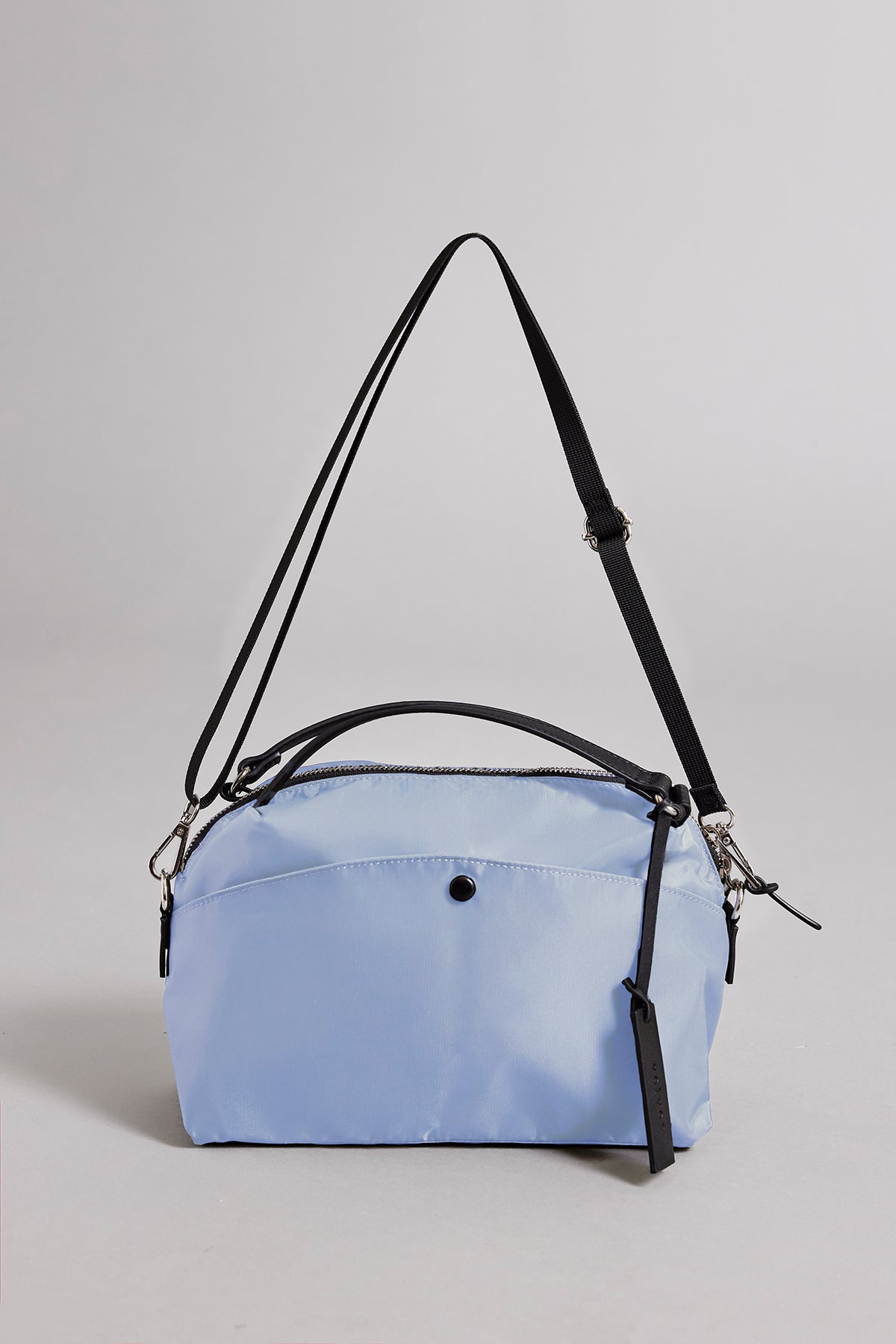   The NYLON CROSSBODY BAG by Velvet by Graham & Spencer is a light blue crossbody bag made from durable nylon with a black adjustable strap and front pocket, ideal for everyday use. 