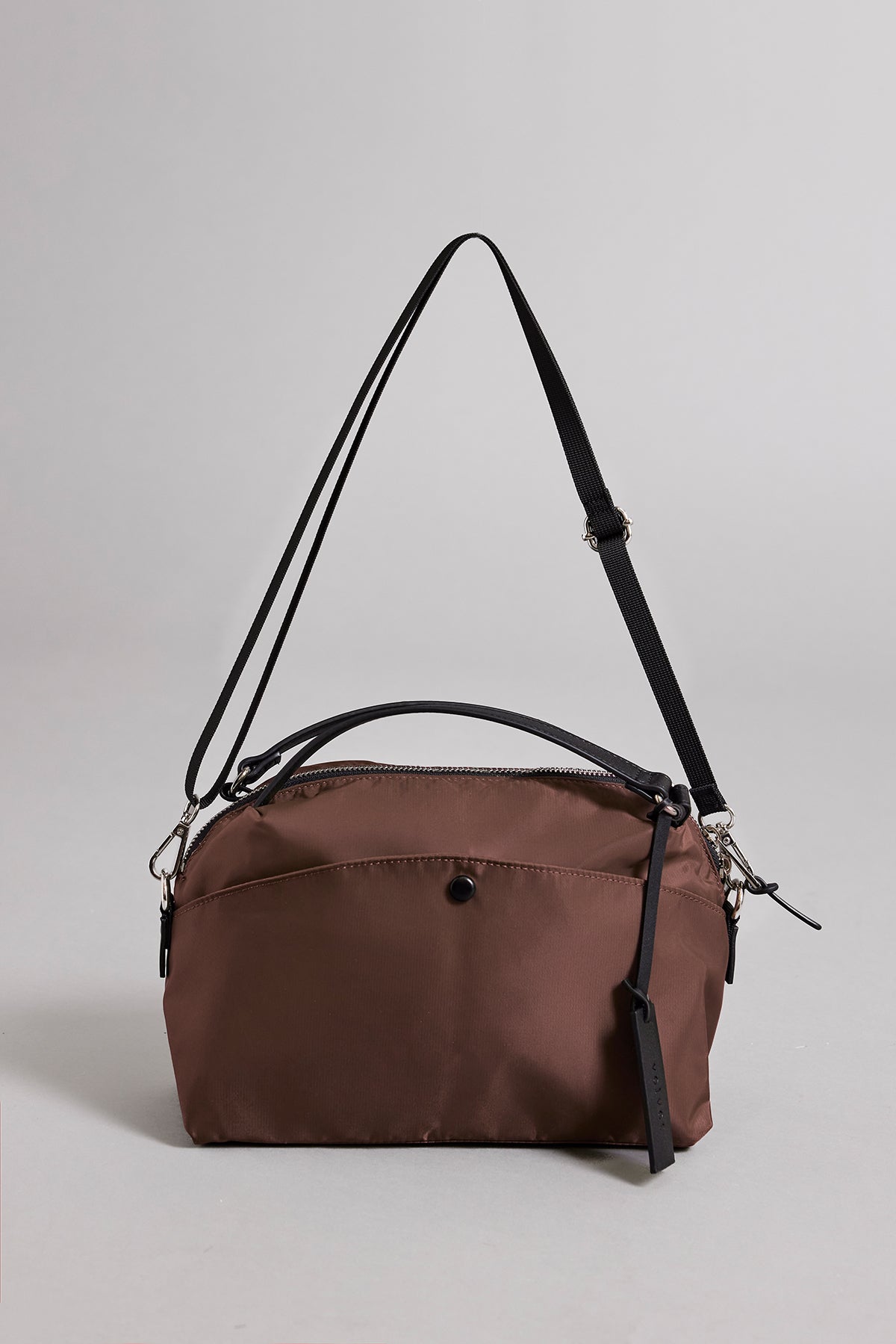   The Velvet by Graham & Spencer NYLON CROSSBODY BAG is a brown and black crossbody crafted from durable nylon with a main zipper compartment, front pocket, and adjustable straps, perfect for everyday use on a simple backdrop. 