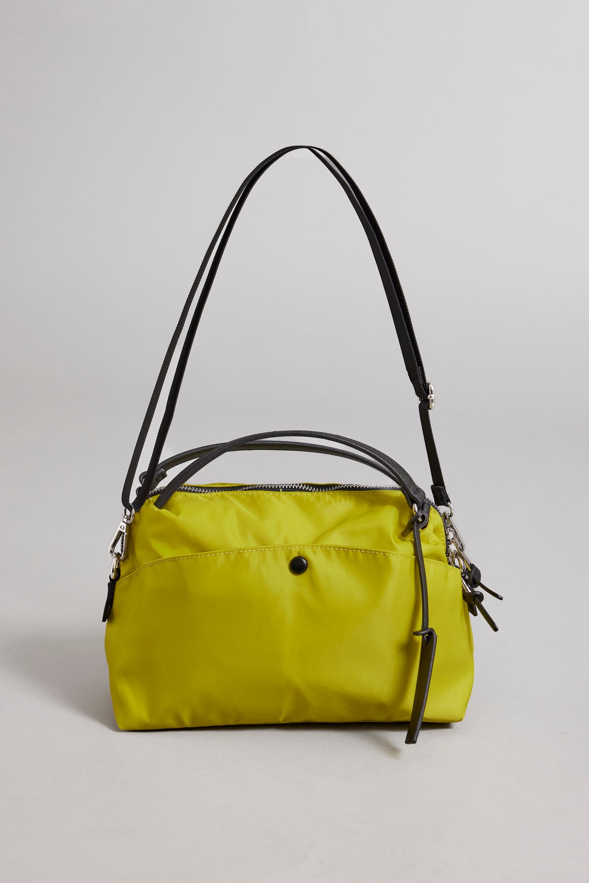   A small lime green NYLON CROSSBODY BAG made of durable nylon with a secure zipper closure and black shoulder straps by Velvet by Graham & Spencer. It is set against a plain gray background. 