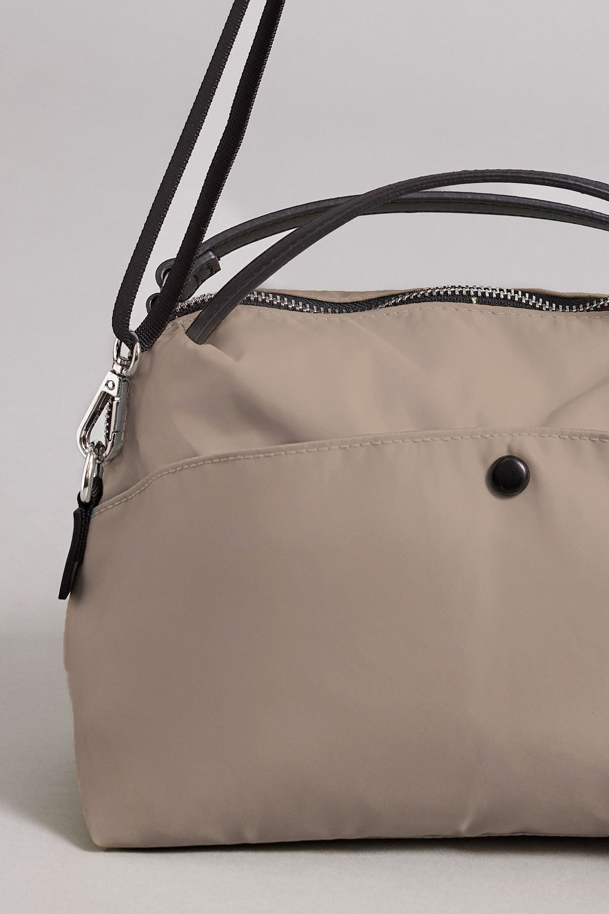 The NYLON CROSSBODY BAG by Velvet by Graham & Spencer features a beige nylon exterior, black button detail, silver zipper, and a black adjustable strap—ideal for everyday use.