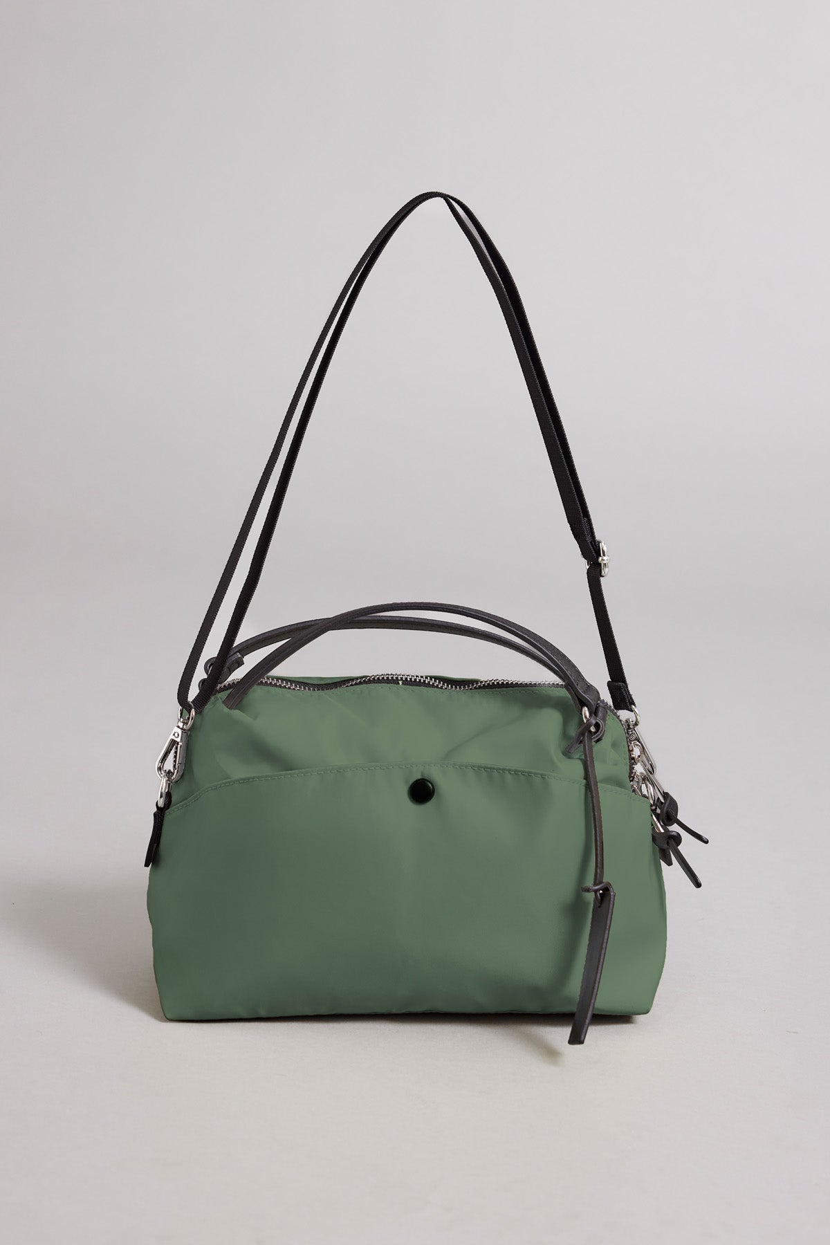 The NYLON CROSSBODY BAG by Velvet by Graham & Spencer is a green nylon handbag featuring black straps and silver hardware, shown against a plain light background. Ideal for everyday use, it offers a zip closure and a front pocket accented with a small black button.-41819569553601