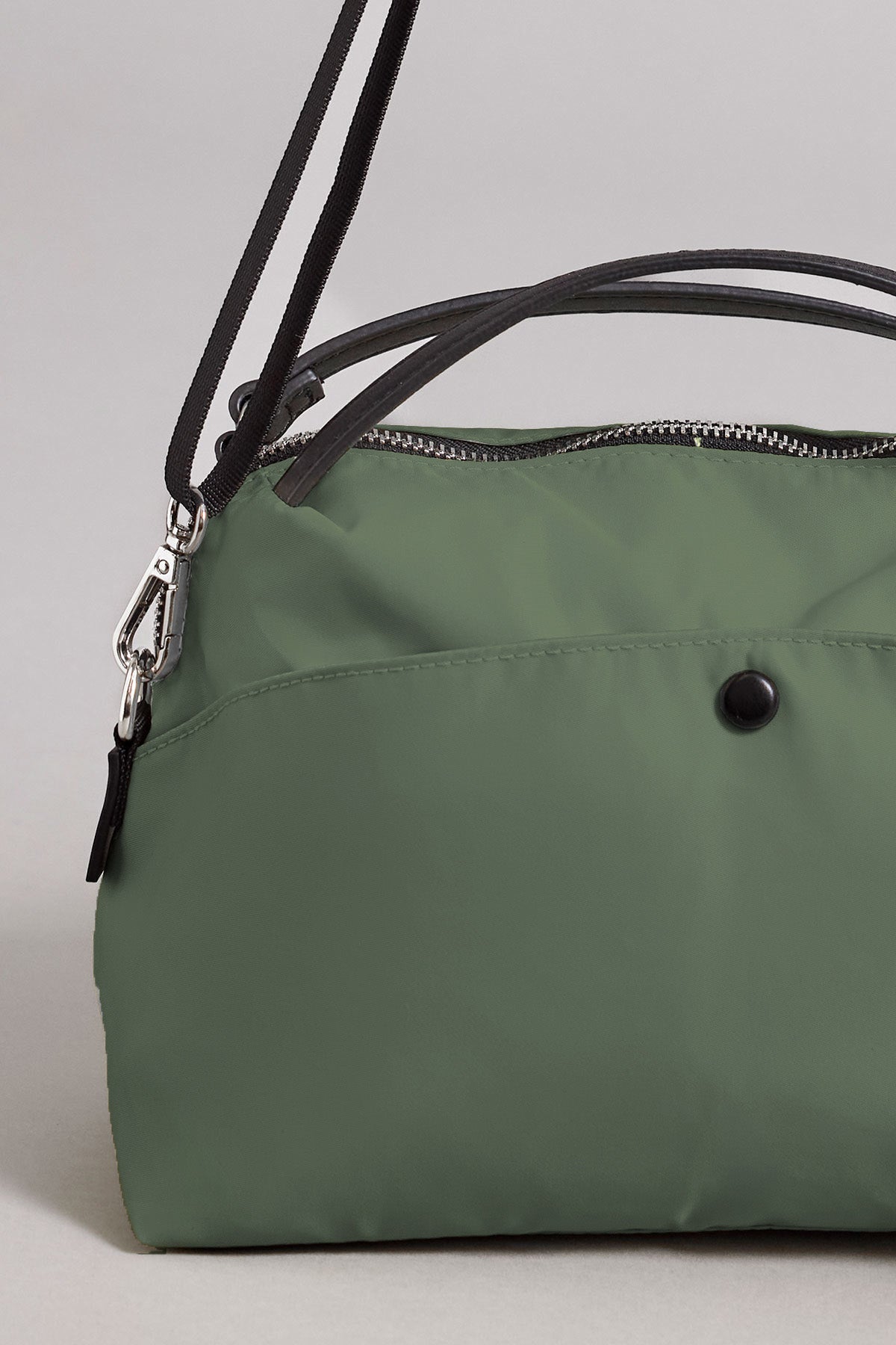 Close-up of the NYLON CROSSBODY BAG by Velvet by Graham & Spencer, featuring a green nylon exterior with black straps, zipper closure, and a distinctive black button detail, set against a plain light background—ideal for everyday use.-41819569520833