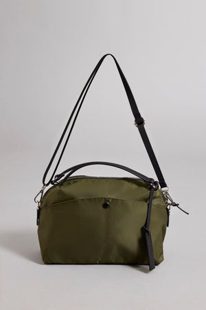 A small olive green Nylon Crossbody Bag by Velvet by Graham & Spencer, crafted from durable nylon, featuring a black adjustable strap, front pocket, and secure zipper closure.