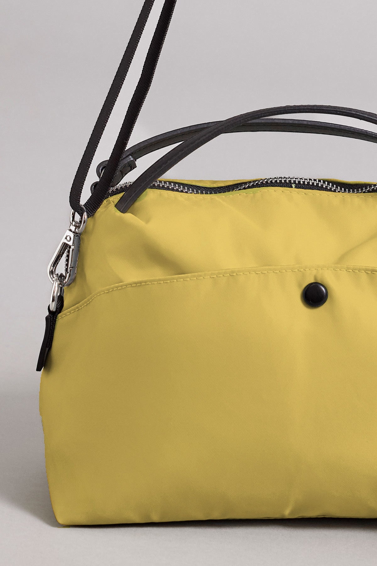 Close-up of the NYLON CROSSBODY BAG by Velvet by Graham & Spencer, featuring yellow nylon material, black handles, a black button detail, and a zipper closure—set against a plain light grey background and ideal for everyday use.