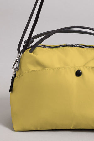 Close-up of the NYLON CROSSBODY BAG by Velvet by Graham & Spencer, featuring yellow nylon material, black handles, a black button detail, and a zipper closure—set against a plain light grey background and ideal for everyday use.