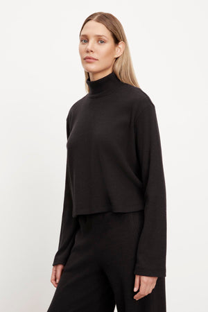 A model in a black ALEC BRUSHED RIB MOCK NECK TOP and wide leg pants by Velvet by Graham & Spencer.