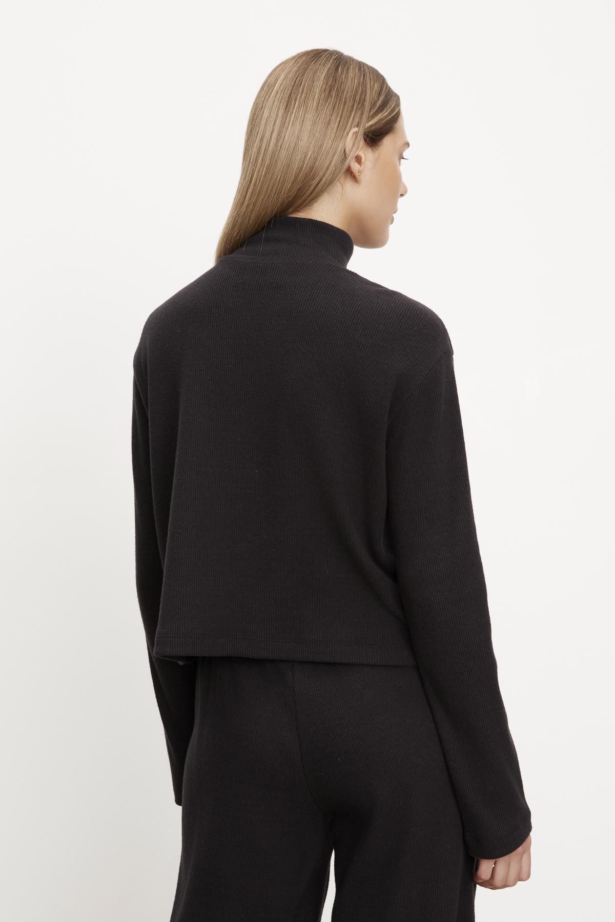   The woman is seen from the back wearing a black ALEC BRUSHED RIB MOCK NECK TOP by Velvet by Graham & Spencer. 