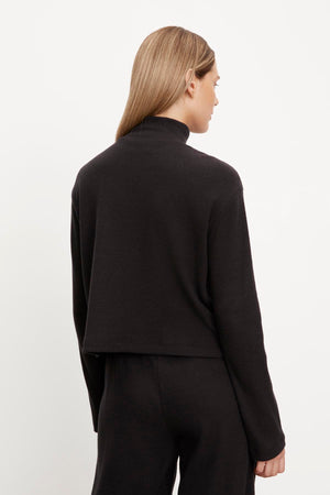 The woman is seen from the back wearing a black ALEC BRUSHED RIB MOCK NECK TOP by Velvet by Graham & Spencer.