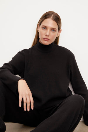 A model wearing a black Velvet by Graham & Spencer ALEC BRUSHED RIB MOCK NECK TOP and sweatpants.