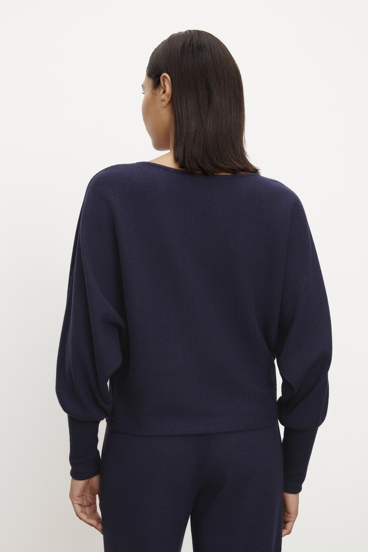 The back view of a woman wearing a Velvet by Graham & Spencer MACKAY BRUSHED RIB TOP sweater and pants.-35702094758081