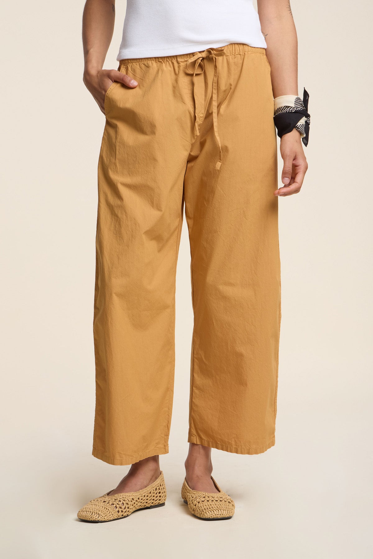 Person wearing the ALLEGRA PANT by Velvet by Graham & Spencer in mustard yellow cotton poplin, styled with a white top, straw slip-ons, and a black-and-white bandana on their wrist.