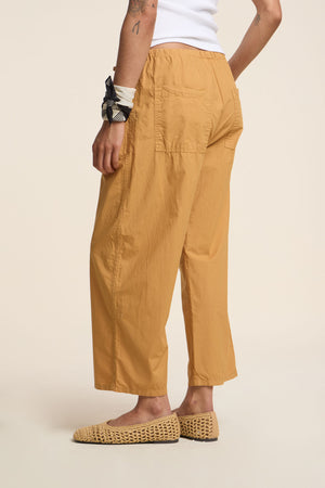 Wearing the ALLEGRA PANT by Velvet by Graham & Spencer—mustard yellow cotton poplin with a cropped length and wide barrel leg—paired with a white top, woven slip-on shoes, and a black and white scarf, against a plain background.