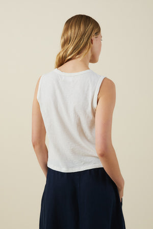 A person with light brown hair is seen from behind, wearing the AMBRIA TANK TOP by Velvet by Graham & Spencer—a sleeveless, boxy white top—paired with dark navy pants against a plain light background.
