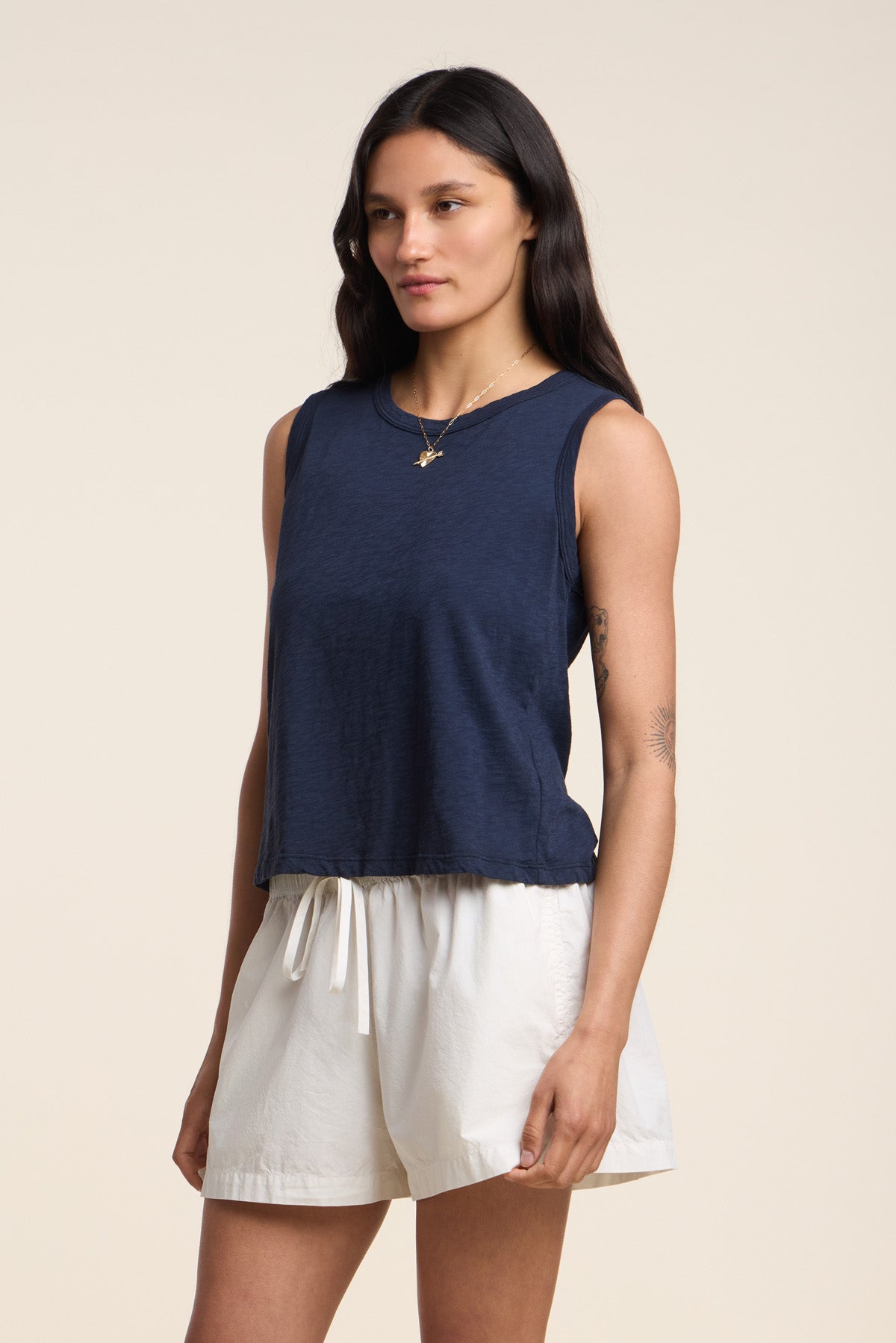 A woman wearing the AMBRIA TANK TOP by Velvet by Graham & Spencer, a navy cotton slub with a boxy swing silhouette, pairs it with white drawstring shorts against a plain light background.-41526896197825