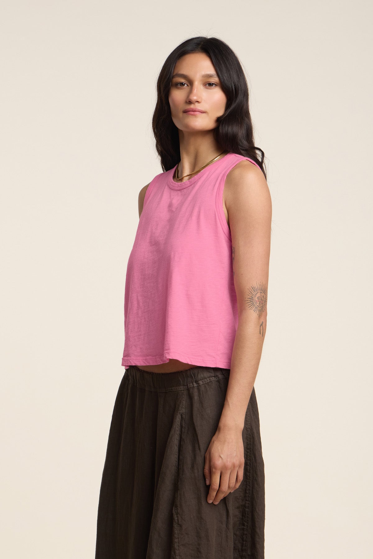 A woman with long dark hair models the AMBRIA TANK TOP by Velvet by Graham & Spencer—a pink cotton slub top paired with a brown skirt, set against a plain light background. A perfect summer wardrobe staple.