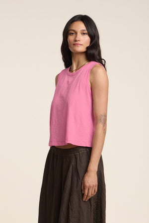 A woman with long dark hair models the AMBRIA TANK TOP by Velvet by Graham & Spencer—a pink cotton slub top paired with a brown skirt, set against a plain light background. A perfect summer wardrobe staple.