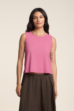 A woman with long dark hair wears the Velvet by Graham & Spencer AMBRIA TANK TOP, a sleeveless pink cropped summer piece with a boxy swing silhouette, paired with a dark brown skirt against a plain light background.