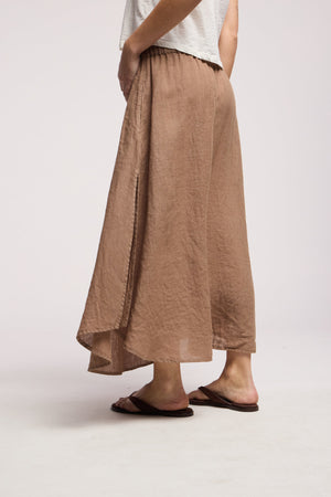 A person wears a white short-sleeve top, the VIRGINIA LINEN SKIRT by Velvet by Graham & Spencer with an elastic waist, and brown sandals, standing against a plain background.