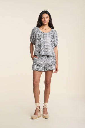A woman poses in a studio wearing the ANGIE TOP by Velvet by Graham & Spencer, paired with matching shorts and light wedge sandals.