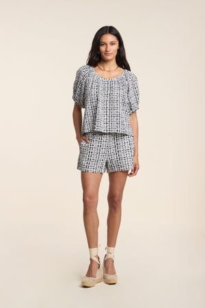 A woman stands wearing the DANIELLA SHORT set by Velvet by Graham & Spencer, featuring a matching short-sleeve blouse and blue and white gingham shorts, paired with light espadrille wedges.