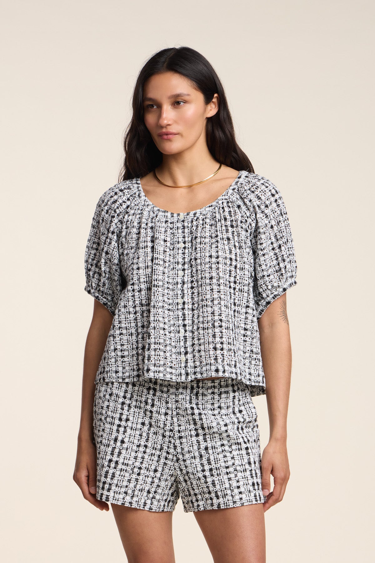 A woman wears the ANGIE TOP by Velvet by Graham & Spencer, a black and white gingham piece, paired with matching shorts, standing against a plain beige background.