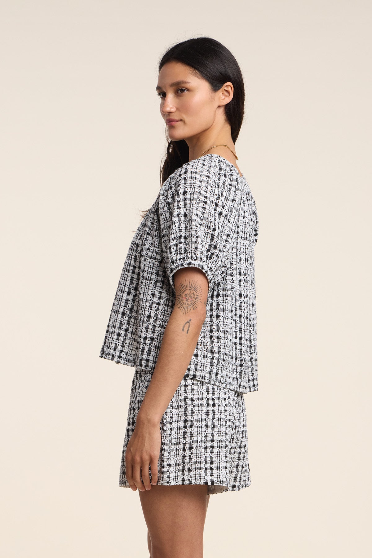 A woman in profile wears the Velvet by Graham & Spencer ANGIE TOP in black and white gingham, paired with matching shorts and displays a visible upper arm tattoo against a plain background.-41526918709441