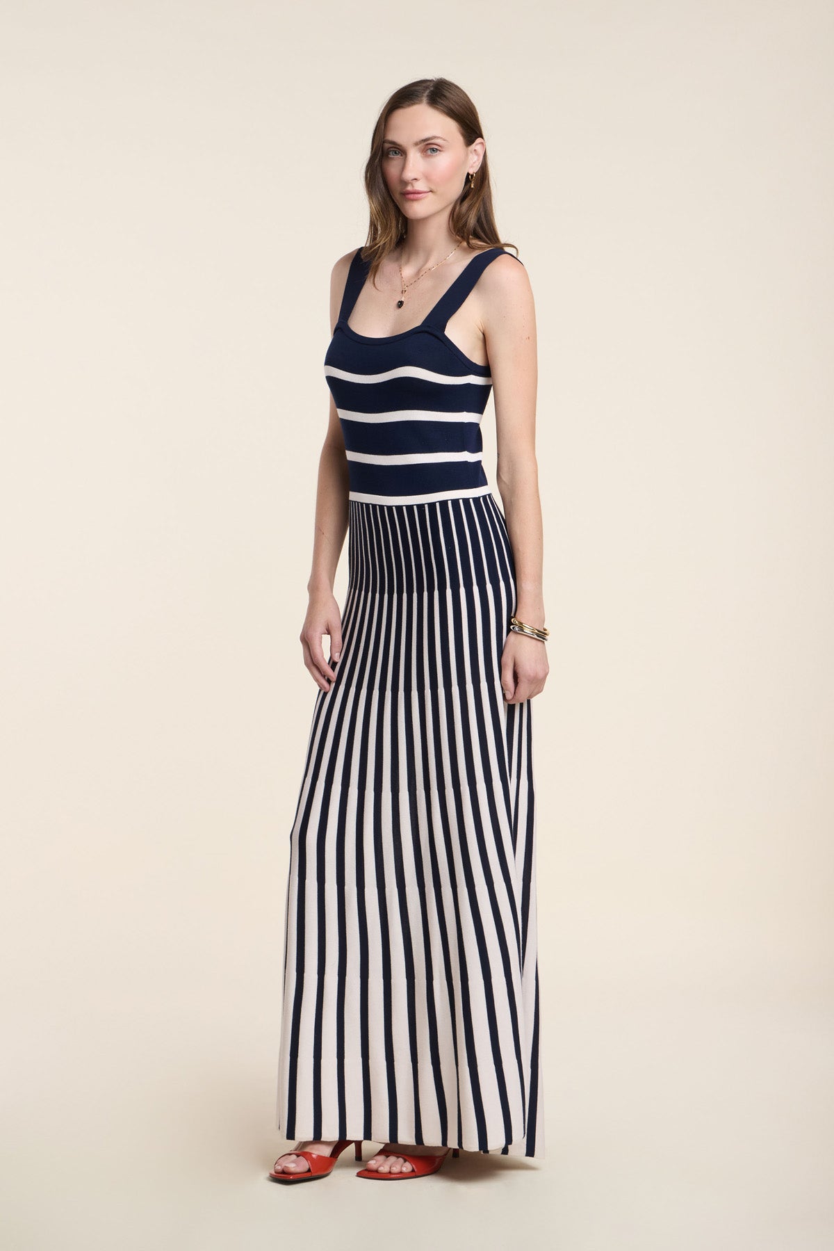A woman wears the AVELINE DRESS by Velvet by Graham & Spencer, a sleeveless knit maxi with a fitted bodice, navy and white horizontal stripes on top, vertical stripes on the skirt, styled with red sandals.-41526920544449