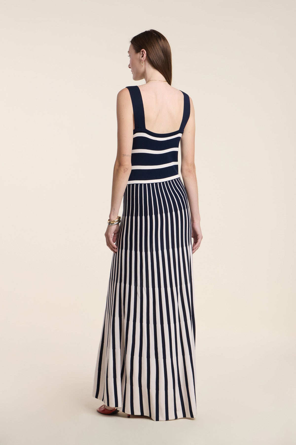 A woman faces away, wearing the AVELINE DRESS by Velvet by Graham & Spencer—a sleeveless knit maxi with a fitted bodice, featuring navy and white stripes horizontally on top and vertically on the skirt for a chic look.-41526920577217
