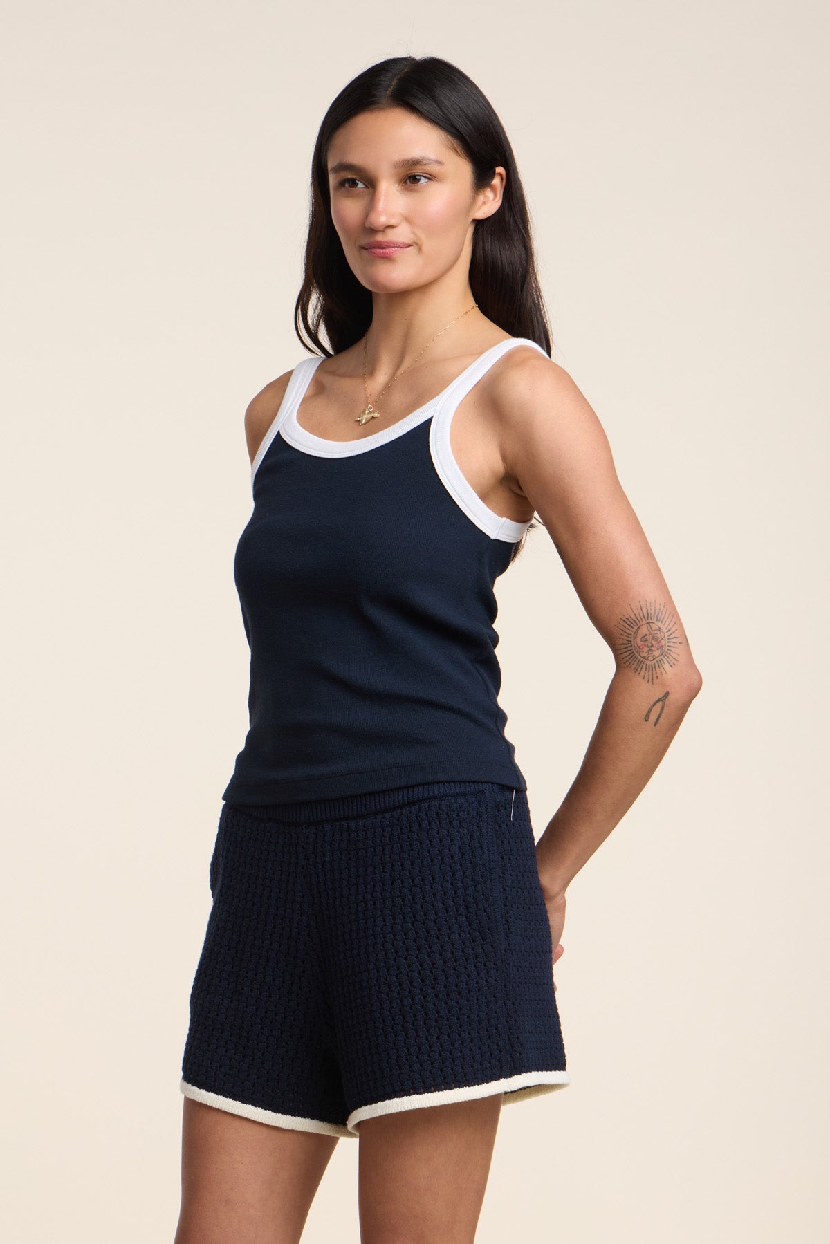 Someone wearing the BELLE TANK TOP by Velvet by Graham & Spencer, a navy ribbed tank with a scoop neckline and white trim, paired with navy shorts, stands against a plain light background.