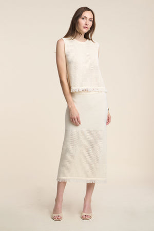 A woman wears the BLYTHE SKIRT by Velvet by Graham & Spencer—a cream cotton mesh pencil skirt with a fringe hem—paired with a matching sleeveless knit top and open-toe heels, set against a neutral background.