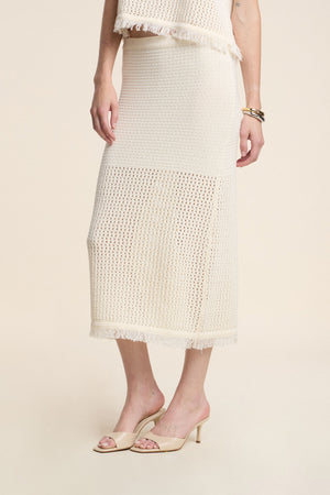A person wearing the BLYTHE SKIRT by Velvet by Graham & Spencer—a cream-colored cotton mesh pencil skirt with a fringe hem—paired with nude heeled sandals and gold bracelets.
