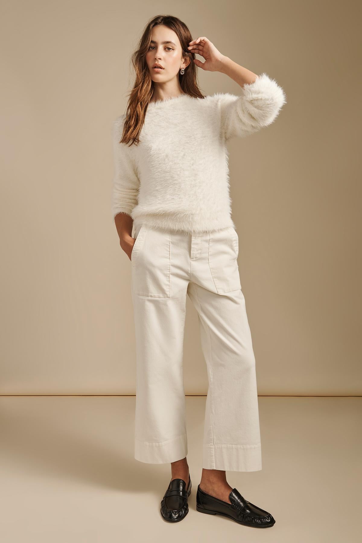 A woman wearing a white fuzzy sweater, white VERA CORDUROY PANT cropped wide-leg utility pants, and black loafers.-46504993095873