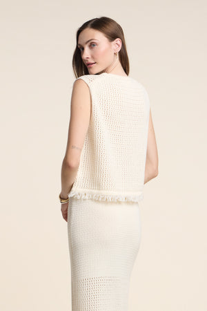 A woman models the COVA SWEATER by Velvet by Graham & Spencer—a sleeveless, cream-colored cotton knit top with a fringe hem—paired with a matching skirt, set against a plain background.